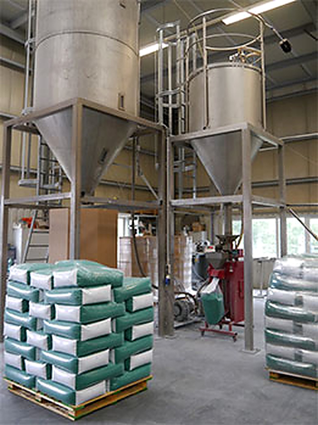 Zwei hohe Silos auf Stahlgerüst in der Halle, darunter die Absackung und palettierte Säcke mit Compound.