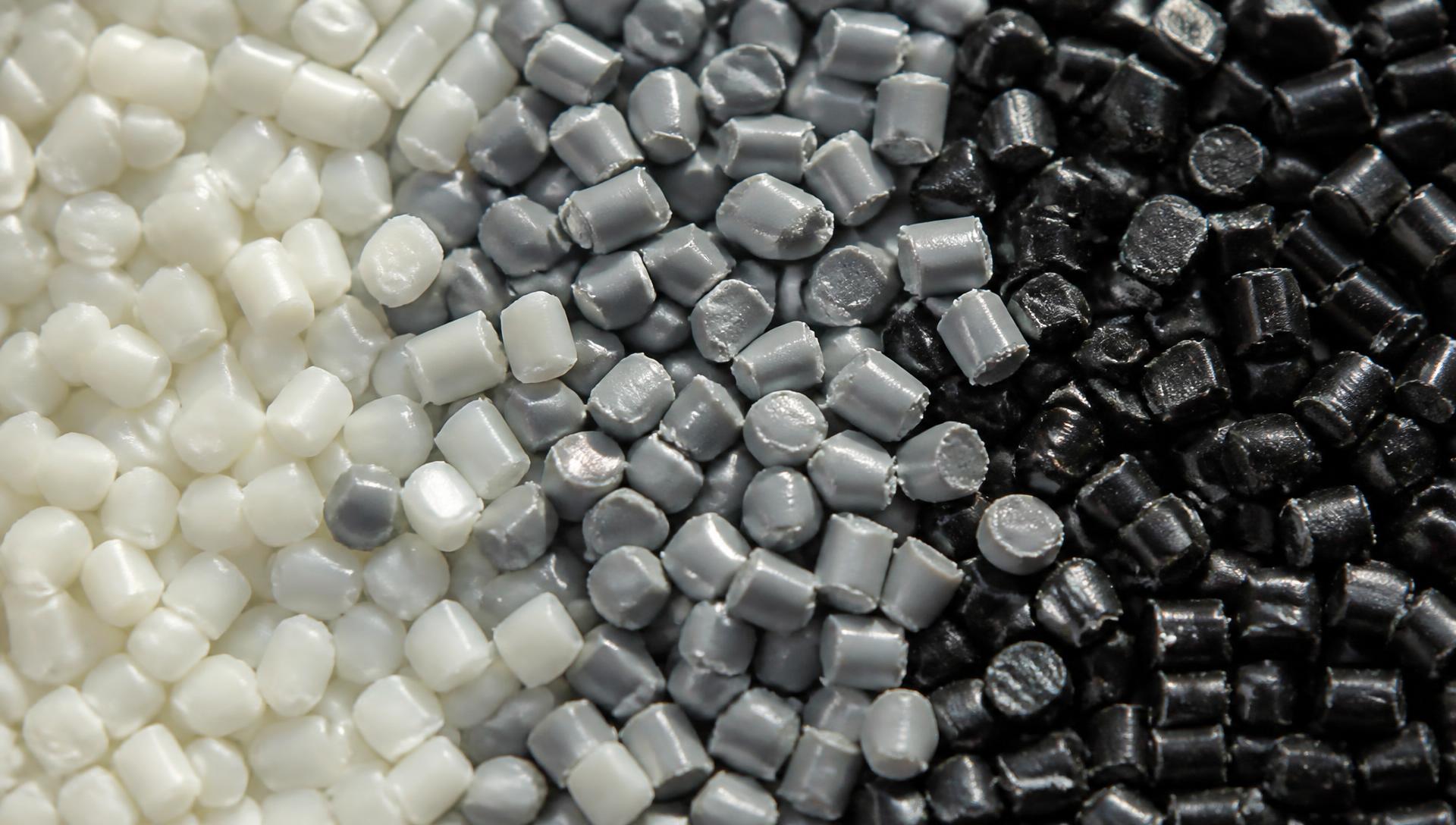 Makroaufnahme von gemischtem technischem Granulat in Naturweiß, Grau und Schwarz nebeneinander.