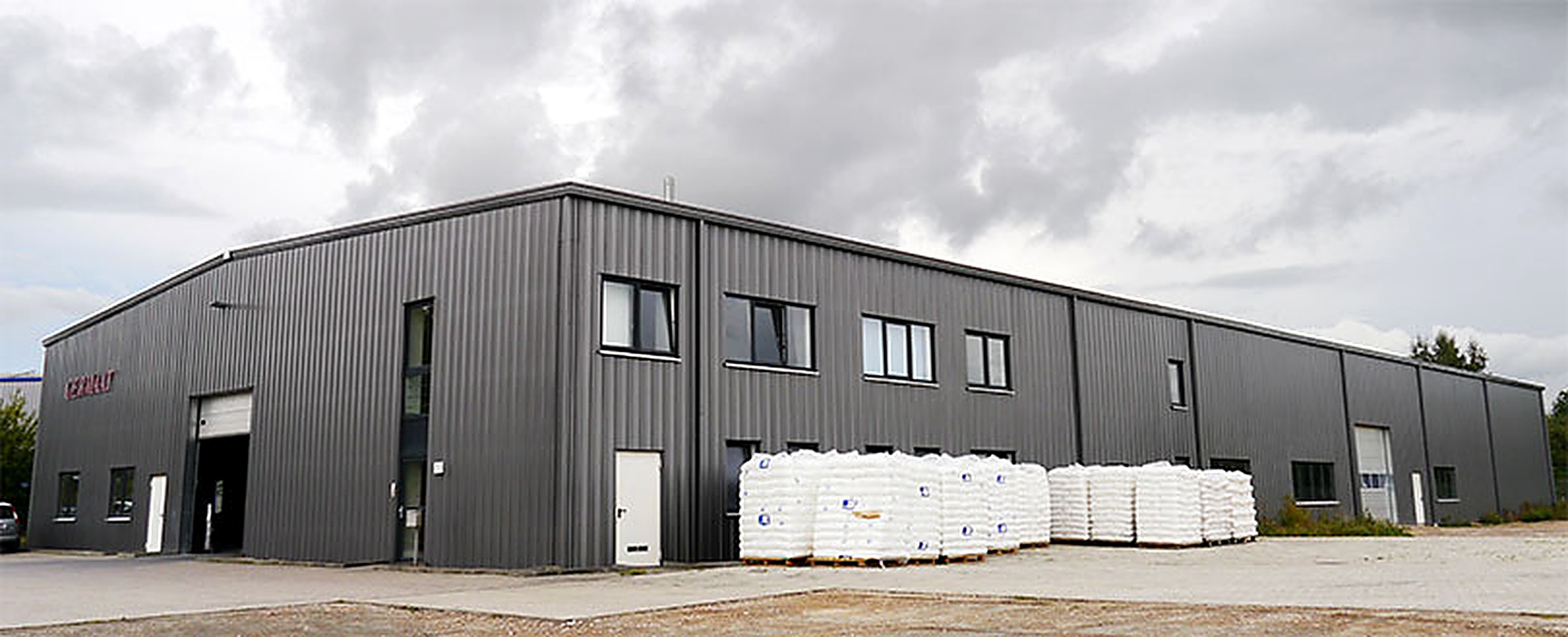 Die dunkelgraue Produktionshalle von GERMAAT Polymer in der Robert-Bunsen-Straße in Schwerin, davor palettierte Säckeware.